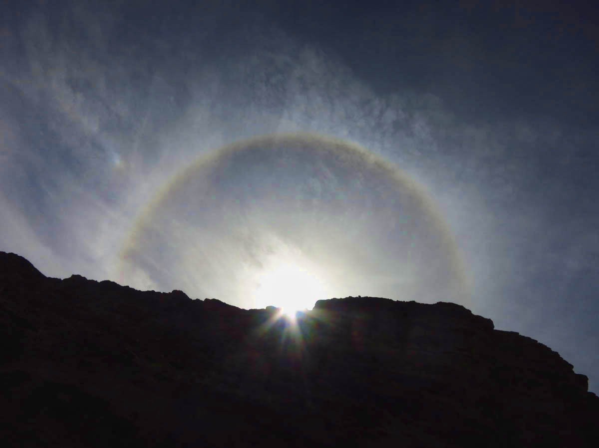 An ice halo around the sun, peeking over a cliff.  This is my first time seeing such a "rainbow" around the sun.